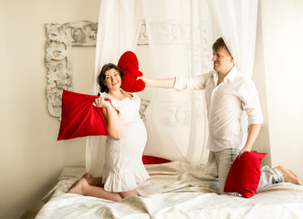 pregnant woman having pillow fight with husband on bed with bald © Kyrylo Ryzhov