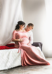 pregnant couple sitting on bed with baldachin next to window © Kyrylo Ryzhov