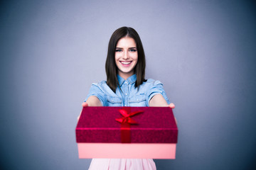 Smiling woman giving a gift box at camera