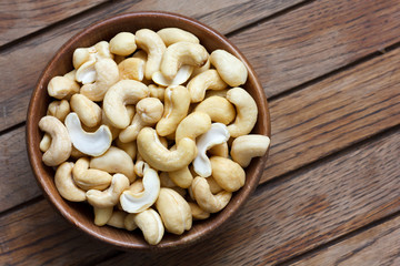 Wooden bowl of cashew nuts from above. On dark wood.
