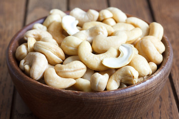 Wooden bowl of cashew nuts from above. On dark wood.