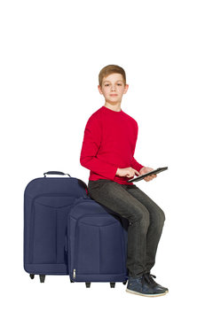 Boy sitting on travel bags holding tablet isolated on white