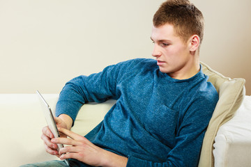Fototapeta premium Young man with tablet sitting on couch at home