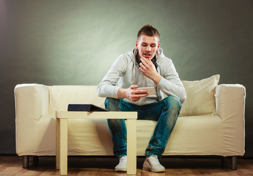 man on couch with headphones smartphone and tablet