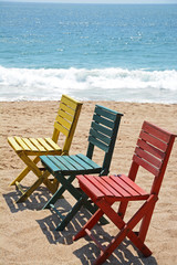 three colorful wooden beach chairs on sand with ocean background