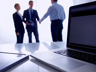 Laptop  computer on  desk , three businesspeople standing in the