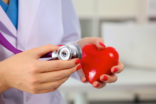 Doctor with stethoscope examining red heart, isolated on white