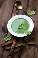 Spinach cream-soup with croutons over dark wooden background