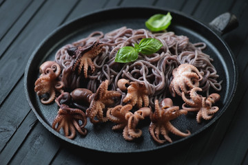 Frying pan with black rice vermicelli and octopuses, close-up