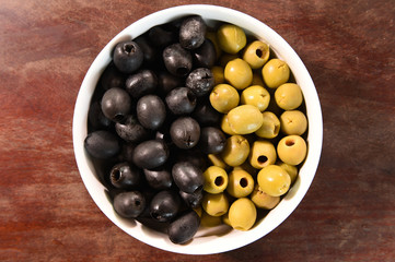 green and black olives in white bowl on wooden background