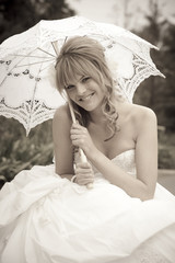 Pretty young bride sitting under lace parasole smiling