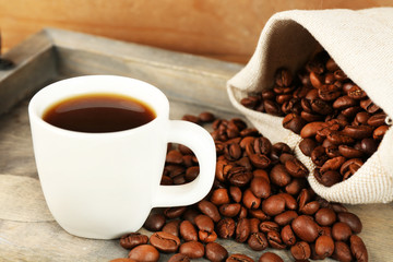 Cup of coffee with beans on tray and rustic wooden background