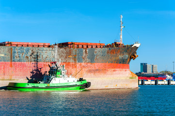 Small tugboat assisting bulk cargo ship in Lithuanian harbor