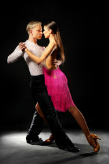 Beautiful couple of professional artists dancing on black background