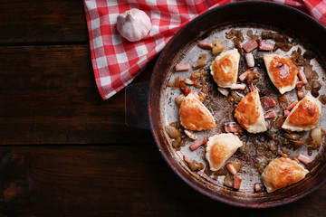 Fried dumplings with onion and bacon in frying pan,