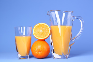 Glass and pitcher of orange juice on blue background