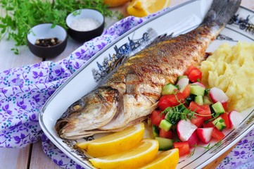 Fried fish served with mashed potato, lemon and vegetables salad
