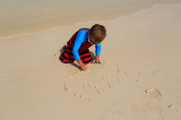 little boy drawing family on the beach