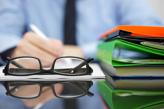 Blurred Businessman Is Writing Document, Focus On Glasses And Fo