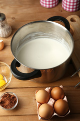 Preparation cream with eggs in pan on wooden background