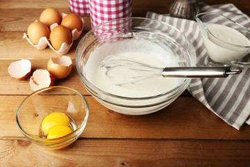 Preparation cream with eggs in glass bowl on wooden background
