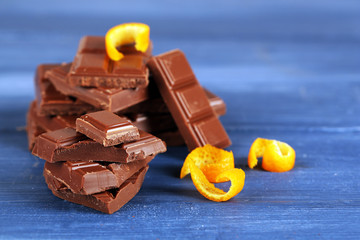 Pieces of chocolate with orange peels on color wooden