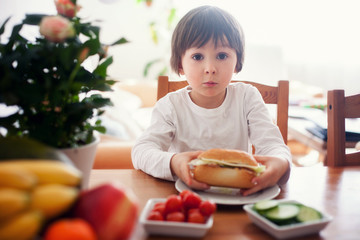 Beautiful little boy, eating sandwich at home, vegetables on the