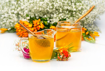 Two Honey jars with stick and flowers near. Isolated white