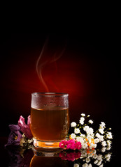Cup of hot tea. Tea Steam. Flowers near. Red Spotlight