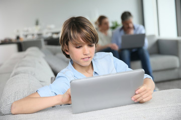 Teenage boy websurfing on tablet, parents in background