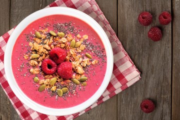 Raspberry smoothie bowl on wood with checkered cloth