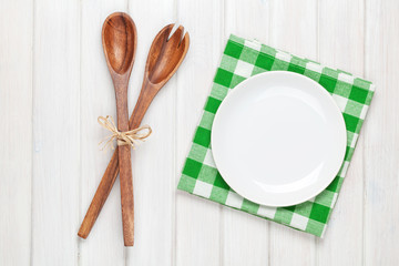 Empty plate and kitchen utensils over wooden table background
