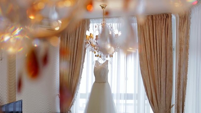 Elegant white wedding dress hanging on a crystal chandelier.