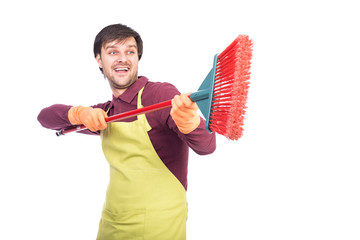 Happy young man with apron and gloves playing with a broom durin