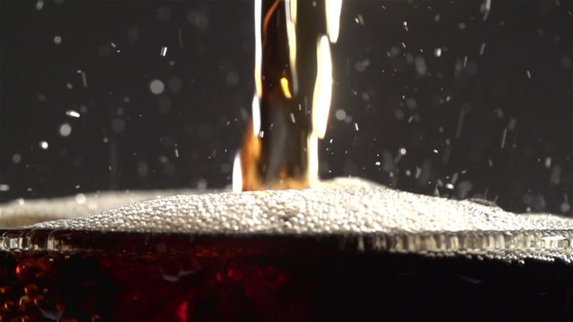 Cola carbonated drink pouring in glass with splash. Slow motion
