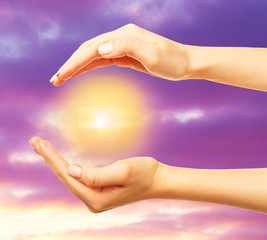 Woman holding sun in hands on sky background