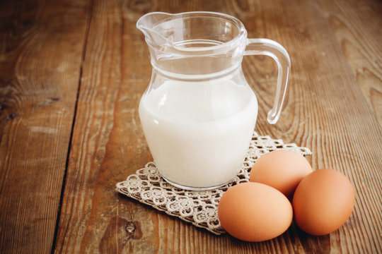 milk in jug and eggs on wooden surface