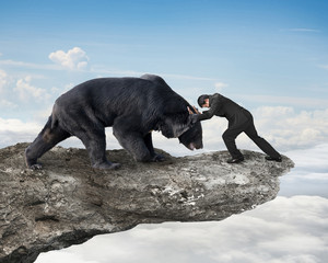 Businessman fighting against black bear on cliff with sky clouds
