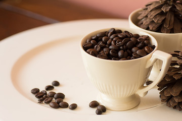 Coffee beans in cup on white plate.
