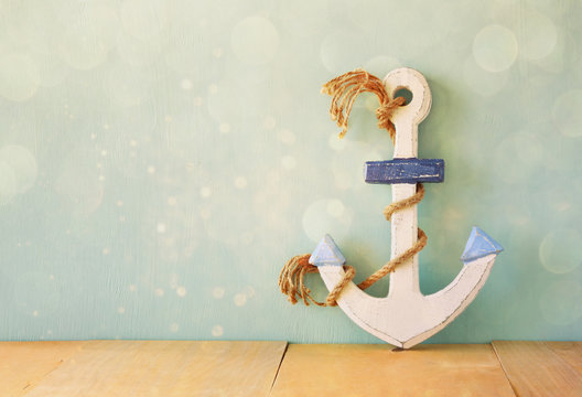 old nautical anchor on wooden table over wooden aqua background 