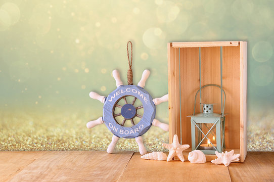 old nautical wood wheel, lantern and shells on wooden table over