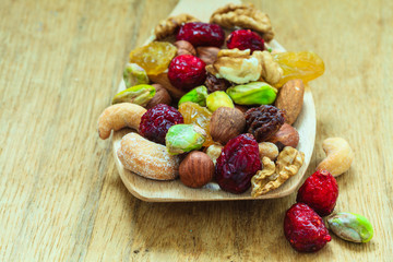 Varieties of dried fruits and nuts on wooden spoon.