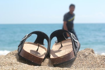 slippers sandals kept next to sea side with a happy man walking