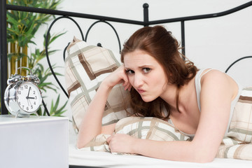 Junge Frau liegt schlaflos im Bett und ist genervt
