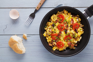 Scrambled eggs in a pan with bacon, onion and tomatoes sprinkled