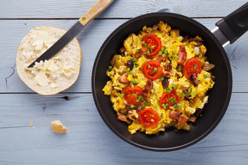 Scrambled eggs in a pan with bacon, onion and tomatoes sprinkled