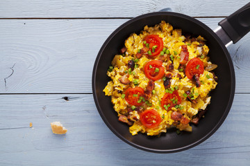 Scrambled eggs in a pan with bacon, onion and tomatoes sprinkled