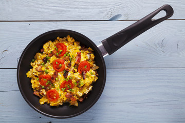 Scrambled eggs in a pan with bacon, onion and tomatoes sprinkled