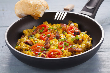 Scrambled eggs in a pan with bacon, onion and tomatoes sprinkled