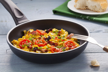 Scrambled eggs in a pan with bacon, onion and tomatoes sprinkled